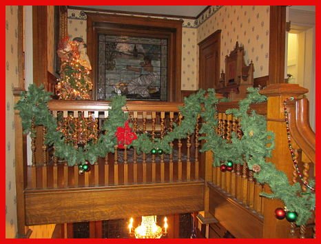 Holiday decorated upstairs staircase with stained glass window in background at the Lawrence County Historical Society.