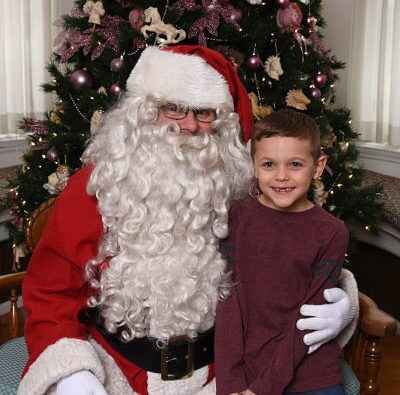 Child standing beside a sitting Santa Claus.