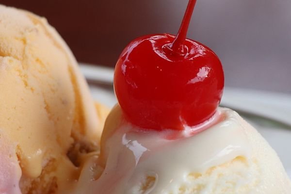 Close up photo of red cherry on vanilla ice cream.