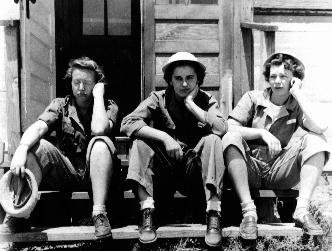 WWII women in military uniforms sitting on outside door steps while leaning on their elbows.